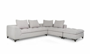 Vista diagonal del Modular con Puff Vitaro Plus Plumas de Aristas. Un diseño moderno con un tapizado suave y elegante, su asiento es acolchado y sus patas discretas en madera color Ceniza. El puff tiene el mismo estilo del sofá y complementa el conjunto.