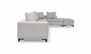Vista lateral del Modular con Puff Vitaro Plus Plumas de Aristas. Este conjunto modular presenta un sofá amplio, con un puff complementario, ambos en un estilo moderno. El diseño destaca por su tapizado suave y elegante, su asiento acolchado y sus cojines de respaldo.