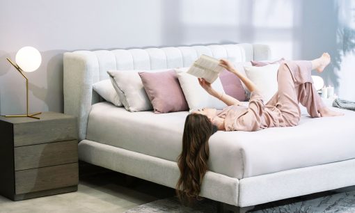 Cama Florencia de la marca Aristas vista en perspectiva diagonal. Presenta un diseño elegante que destaca por su cabecero alto y acolchado de líneas limpias. Tiene una base tapizada en tela suave y patas en madera de estilo clásico.