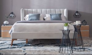 Cama Florencia de la marca Aristas vista en perspectiva frontal. Presenta un diseño elegante con un cabecero alto y de líneas limpias. Tiene un acabado en tela suave y patas en madera de estilo clásico.