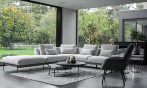Vista diagonal de la Sala En L Modular Maia con puff, de la marca Aristas. Un diseño contemporáneo, con un tapizado en tela suave de color neutro y líneas rectas que aportan elegancia