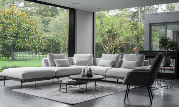 Vista diagonal de la Sala En L Modular Maia con puff, de la marca Aristas. Un diseño contemporáneo, con un tapizado en tela suave de color neutro y líneas rectas que aportan elegancia