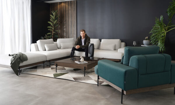 Vista diagonal de la Sala En L Modular Maia con puff, de la marca Aristas. Un diseño contemporáneo y elegante de líneas rectas, con un tapizado en tela suave de color neutro. El puff, con el mismo estilo y material, complementa el conjunto.
