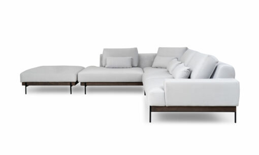 Vista lateral de la Sala En L Modular Maia con puff, de la marca Aristas. Un diseño contemporáneo, tapizado en tela suave de color neutro, base en madera y patas metálicas. El puff, con el mismo estilo y material, complementa el conjunto.