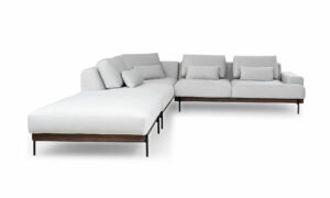 Vista frontal de la Sala En L Modular Maia con puff, de la marca Aristas. El sofá modular presenta un diseño contemporáneo, con un tapizado en tela suave de color neutro y líneas rectas que aportan elegancia. El puff, con el mismo estilo y material, complementa el conjunto.