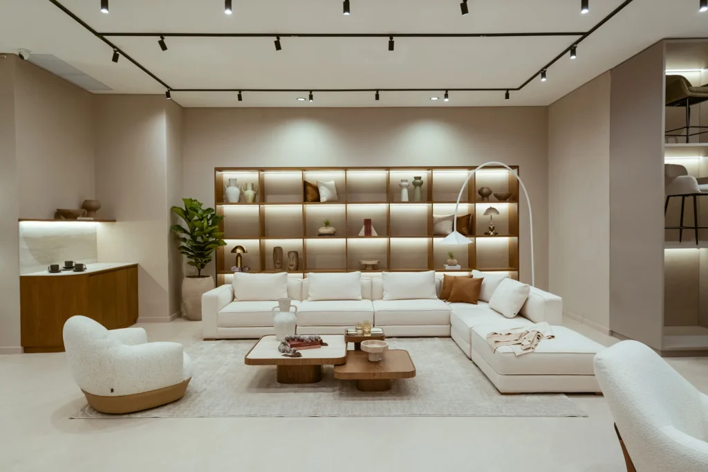 Sala en tonos blancos y crema con sofá modular, sillones bouclé y estantería iluminada en madera, ambientada con luz cálida