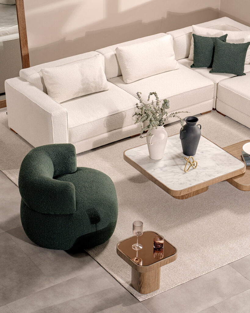 Sofá modular en L en bouclé blanco con cojines verdes, poltrona verde oscuro y mesa de centro en mármol y madera
