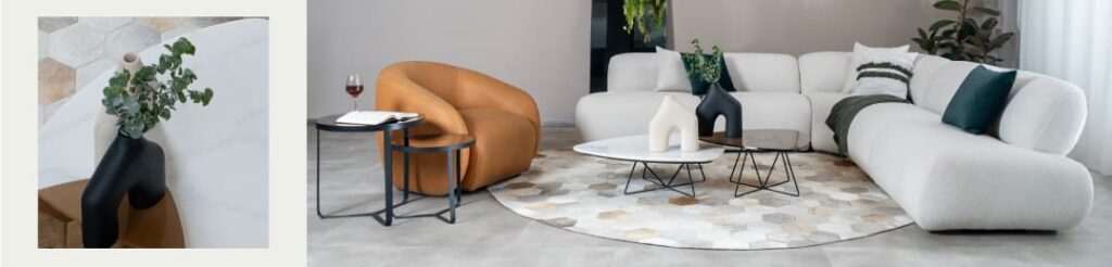 Detalle de jarrón negro sobre mesa de mármol junto a una sala con modular blanco en bouclé, poltrona en cuero caramelo y mesas de centro redondas