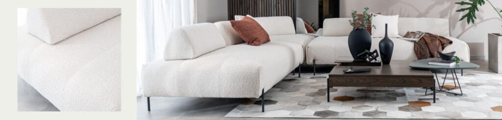 Detalle de tapizado en bouclé crudo junto a una sala con modular blanco, cojín terracota y mesa de centro de madera oscura