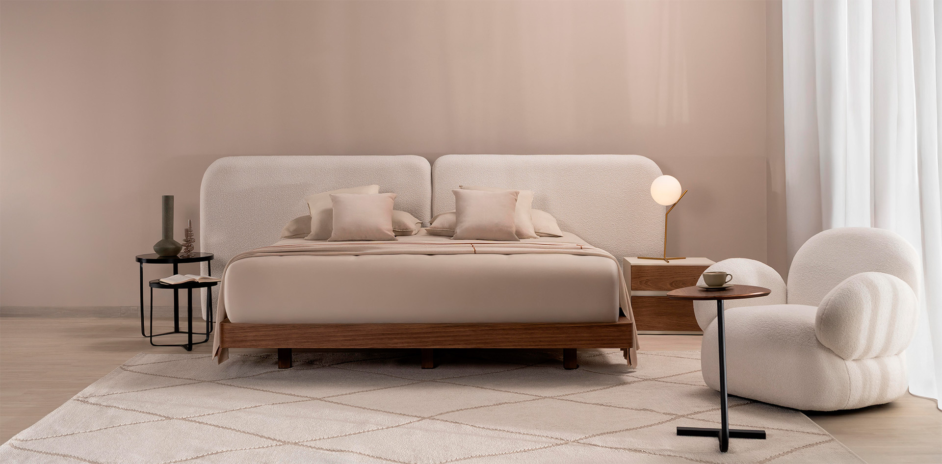 Cama con espaldar en dos paneles de bouclé crudo y base en nogal, con poltrona en bouclé blanco y mesa auxiliar