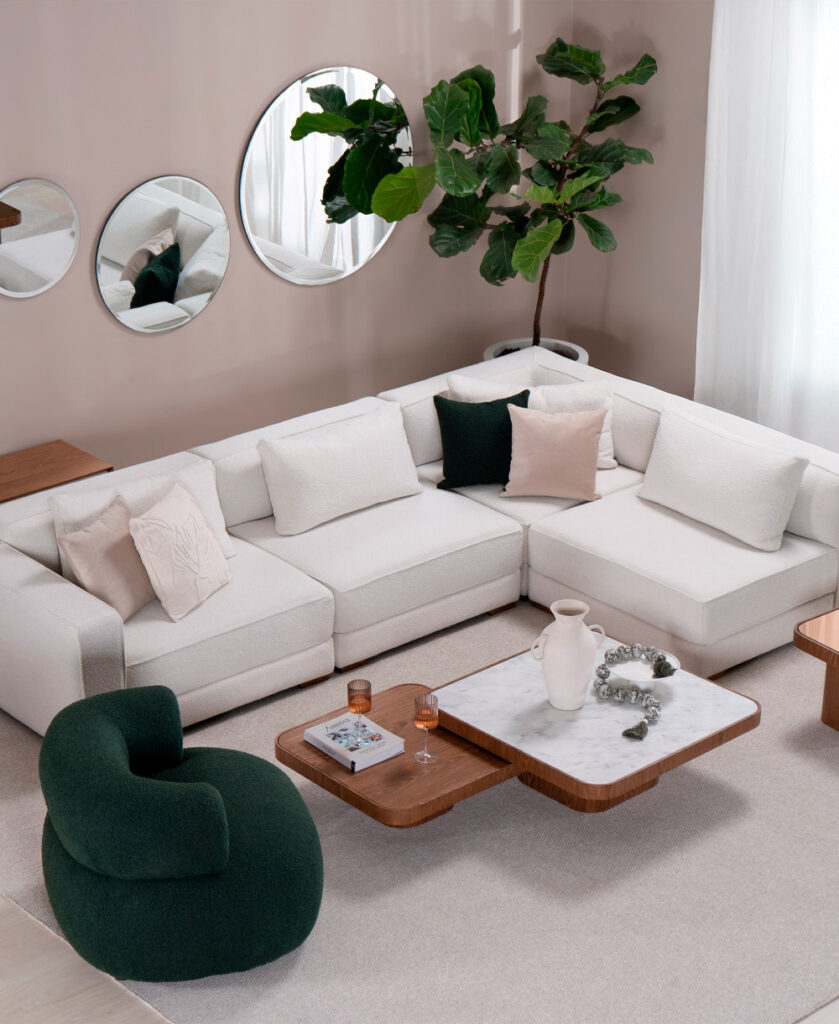 Sala con sofá modular en L en bouclé blanco, poltrona verde y tres espejos redondos, con mesas de centro en madera y mármol
