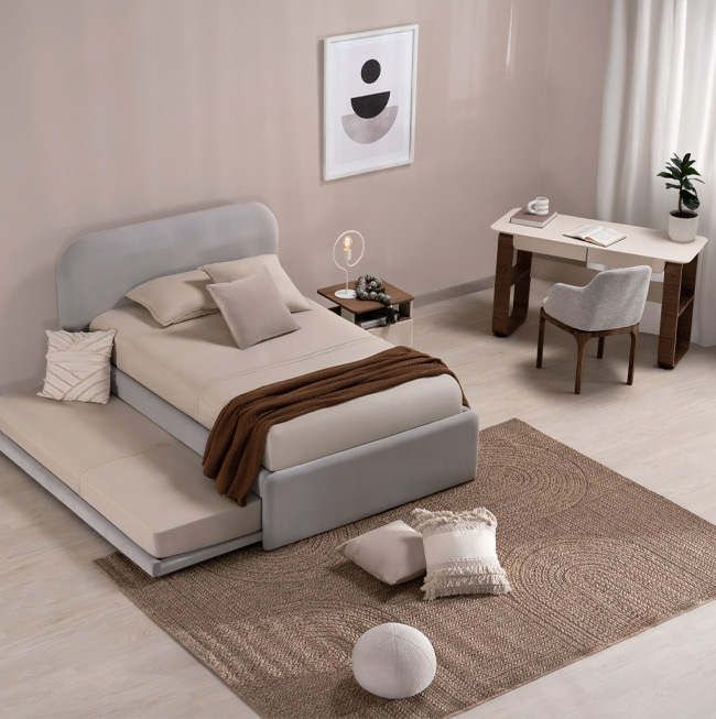 Dormitorio juvenil con cama tapizada en gris y cama auxiliar, escritorio en madera clara y tapete en yute