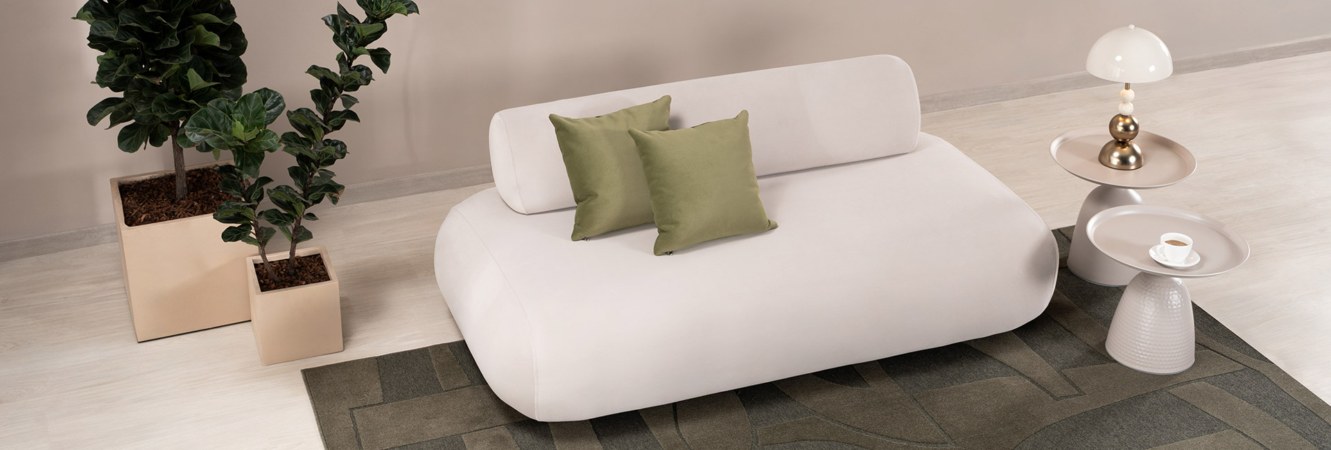 Sofá de líneas curvas tapizado en blanco con cojines verde oliva, junto a materas con plantas y mesas auxiliares sobre un tapete verde