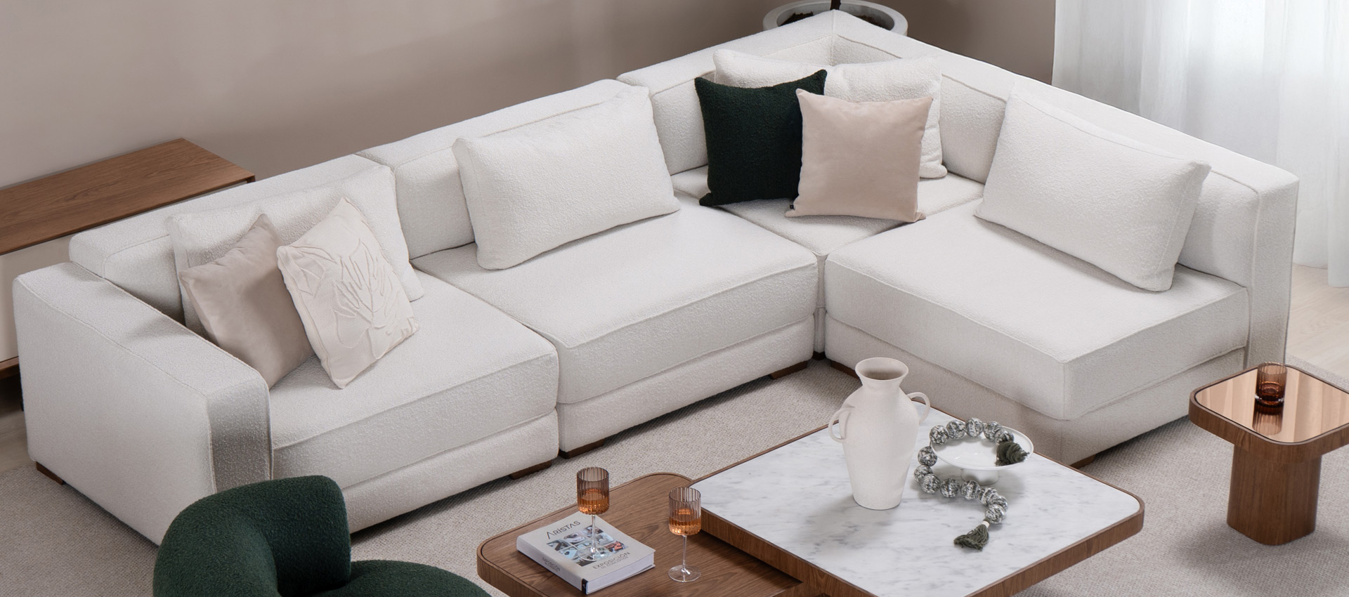 Sofá modular en L en bouclé blanco visto desde arriba, con cojines verdes y mesa de centro en mármol y nogal