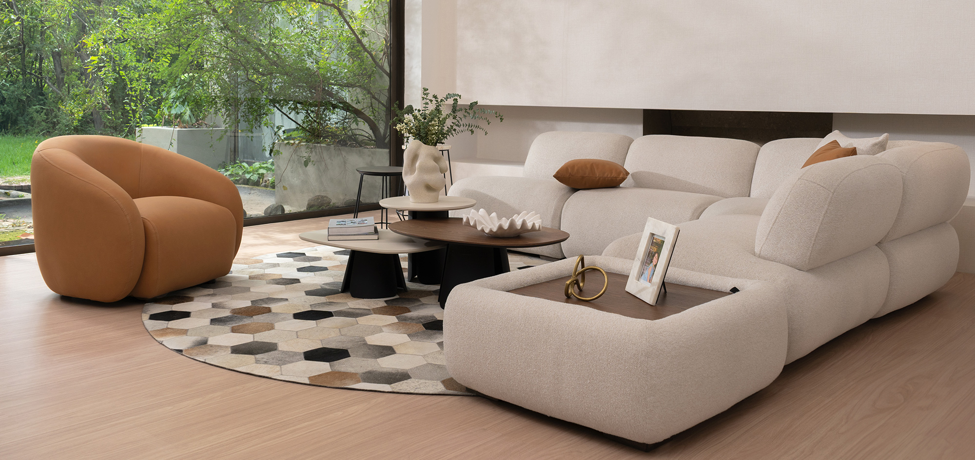 Sala con sofá modular en bouclé crudo y otomana, poltrona en cuero cognac y tapete hexagonal en pieles, abierta al jardín