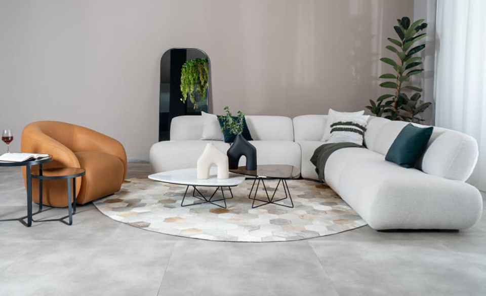 Sala con sofá modular en L en bouclé blanco, poltrona color caramelo y mesas de centro blancas, sobre un tapete circular de pieles