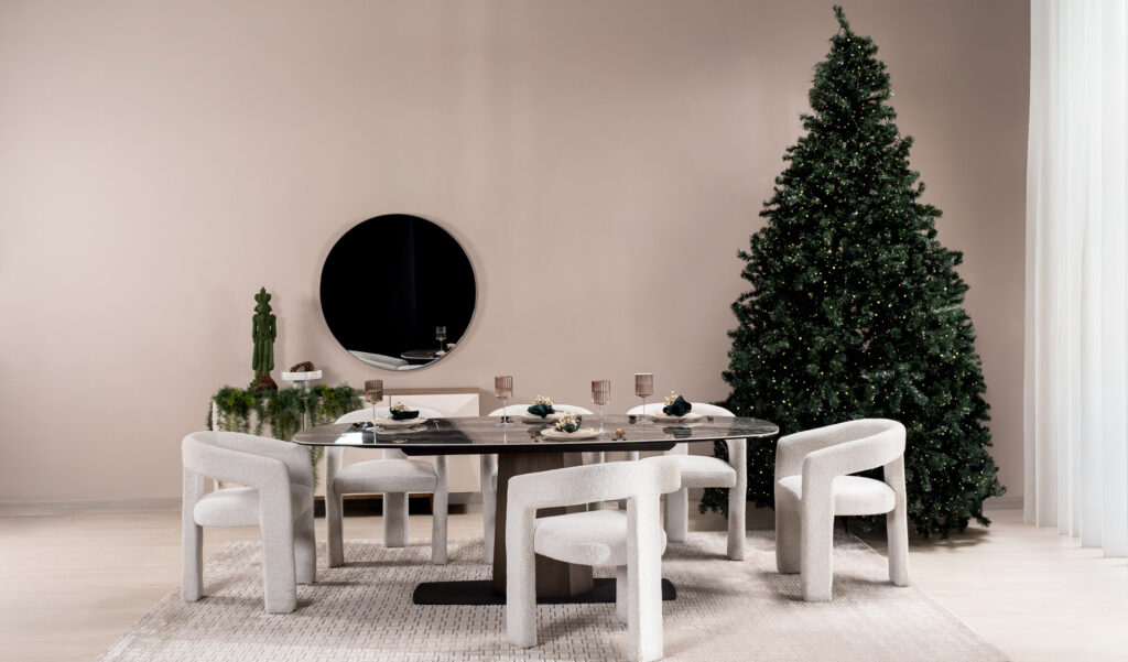 Comedor ovalado en piedra oscura con sillas escultóricas en bouclé blanco, servido junto a un árbol de Navidad