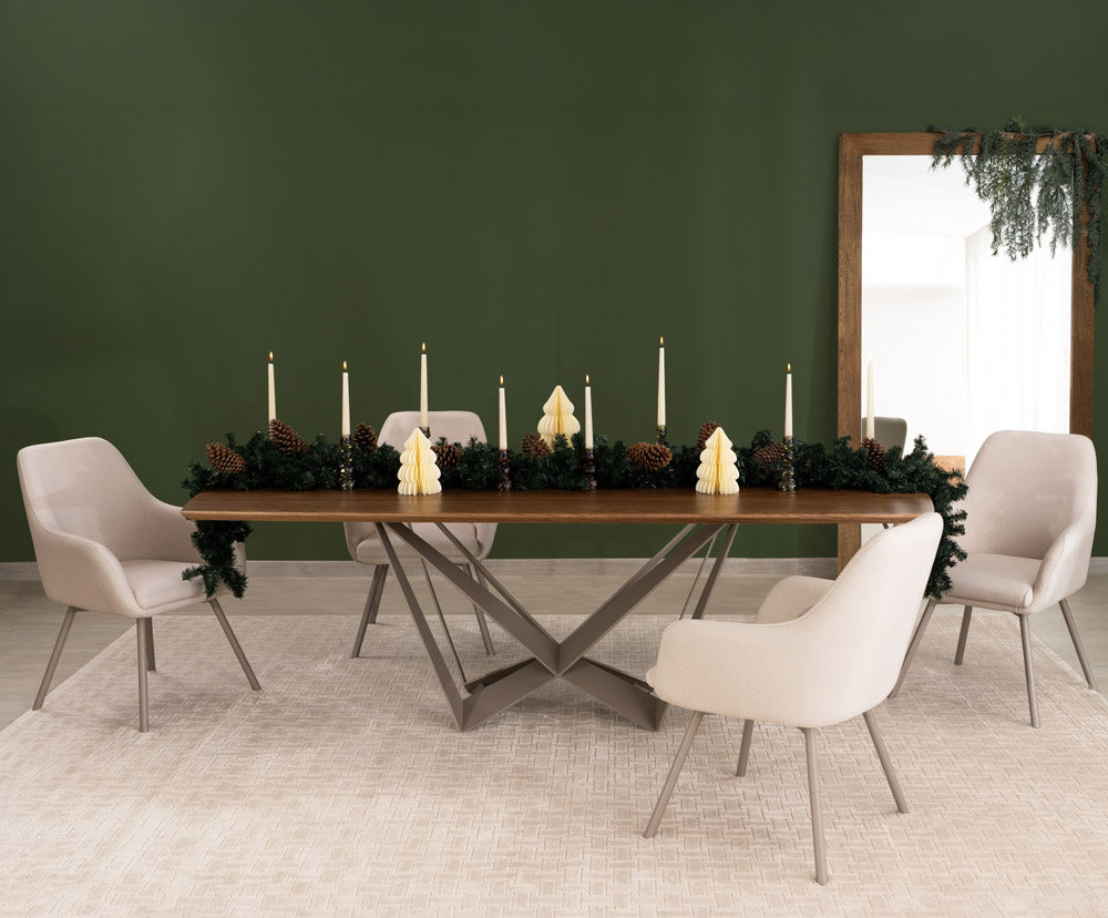 Comedor rectangular en nogal sobre muro verde oscuro, con guirnalda de velas y piñas, sillas en tono crudo y espejo de piso