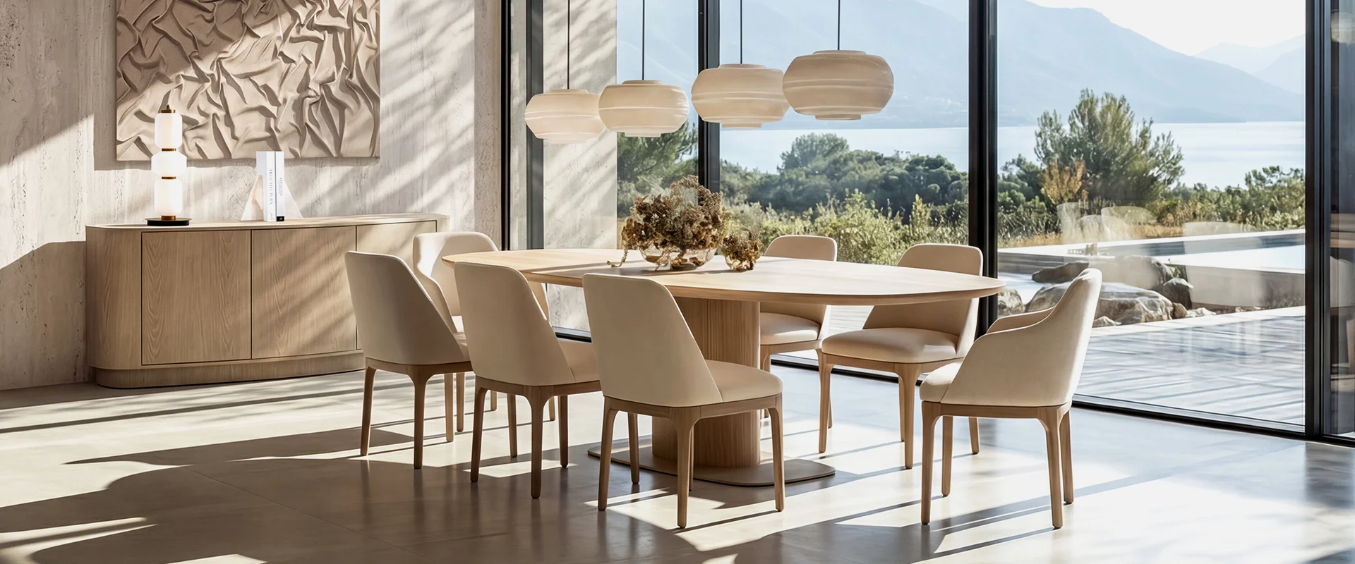 Comedor con mesa ovalada de madera, sillas tapizadas beige y lámparas colgantes orgánicas frente al mar
