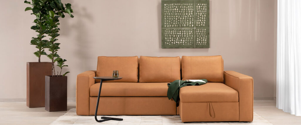 Sala con sofá en L en cuero color caramelo y chaise longue, junto a una obra en tonos verdes y plantas en materas altas