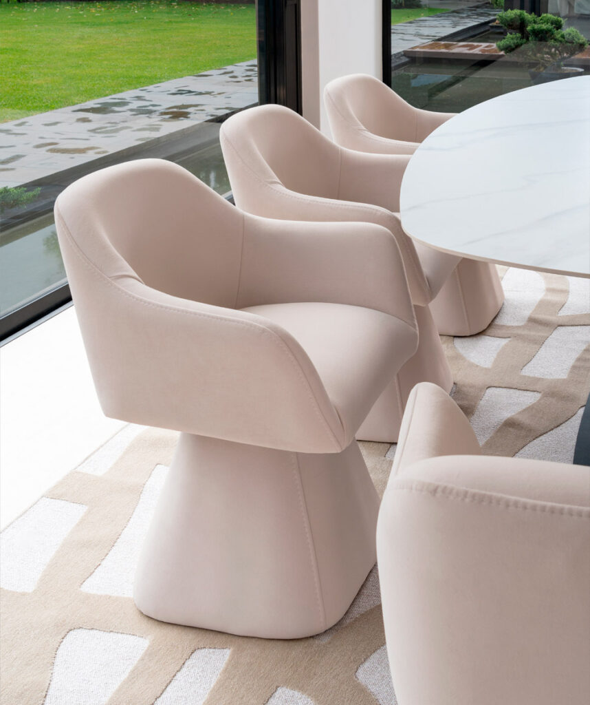 Sillas de comedor Amarai tapizadas en tono nude con base tipo pedestal, junto a una mesa en piedra blanca