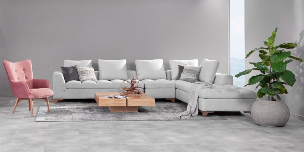 Sala con sofá modular en L gris claro, poltrona rosa, mesa de centro de madera y una planta grande en matera, frente a un muro gris