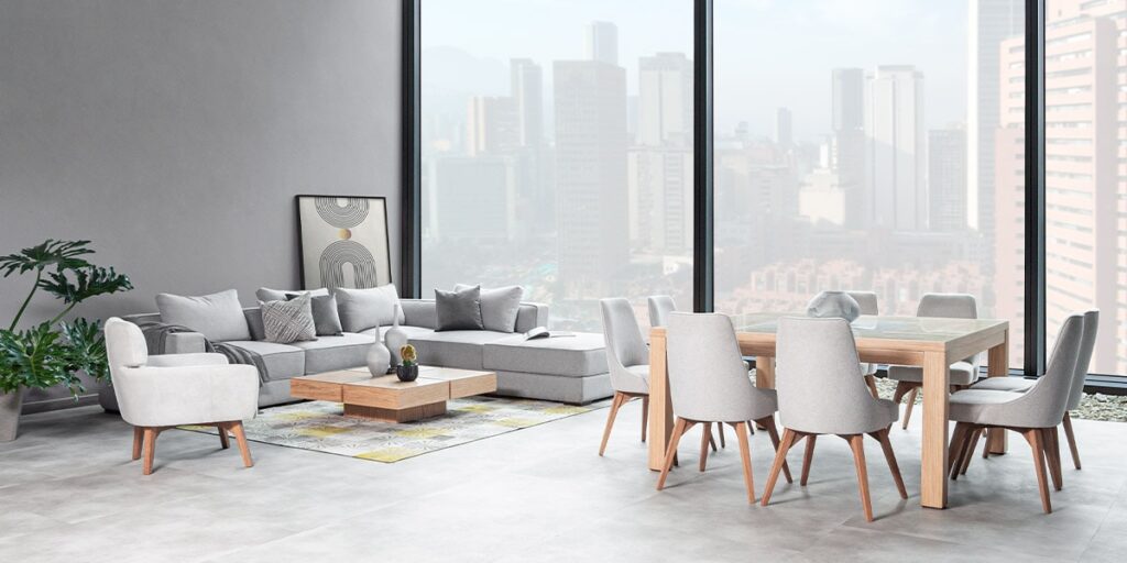 Sala y comedor integrados con sofá modular gris, poltrona crema y comedor de madera clara, frente a ventanales con vista a la ciudad