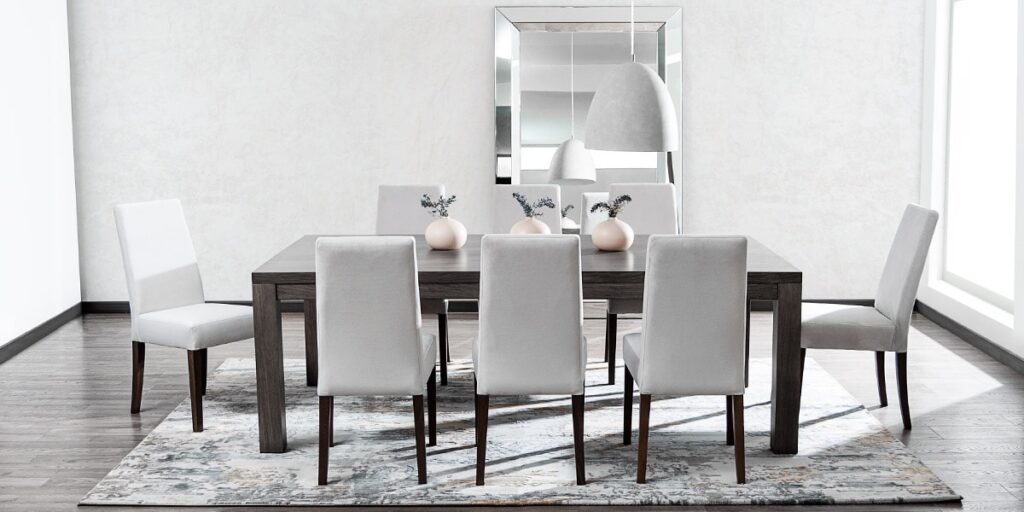 Comedor con mesa de madera oscura y sillas tapizadas en gris claro, con jarrones pequeños y un espejo de marco ancho al fondo