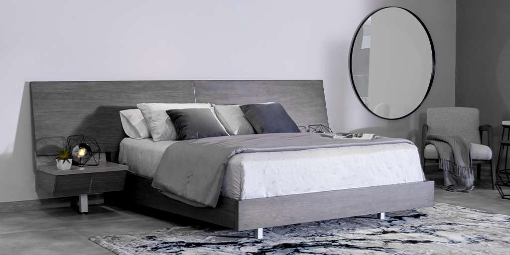 Dormitorio con cama de cabecero amplio en madera gris, mesas de noche flotantes y un espejo redondo con marco negro
