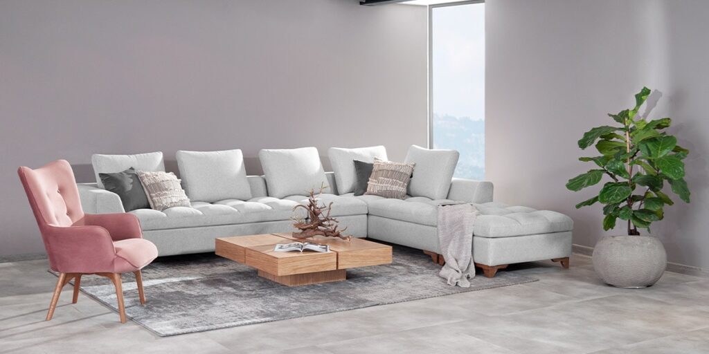 Sofá modular en L gris claro con poltrona rosa, mesa de centro de madera y una planta grande en matera