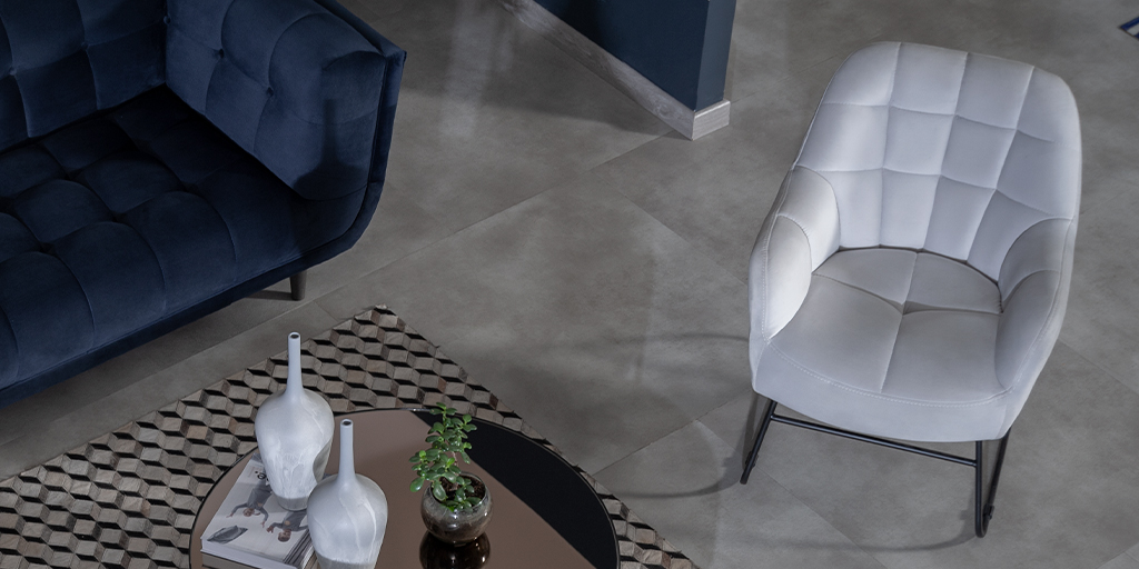 Poltrona blanca capitonada junto a un sofá azul oscuro y una mesa de centro con espejo bronce y jarrones blancos