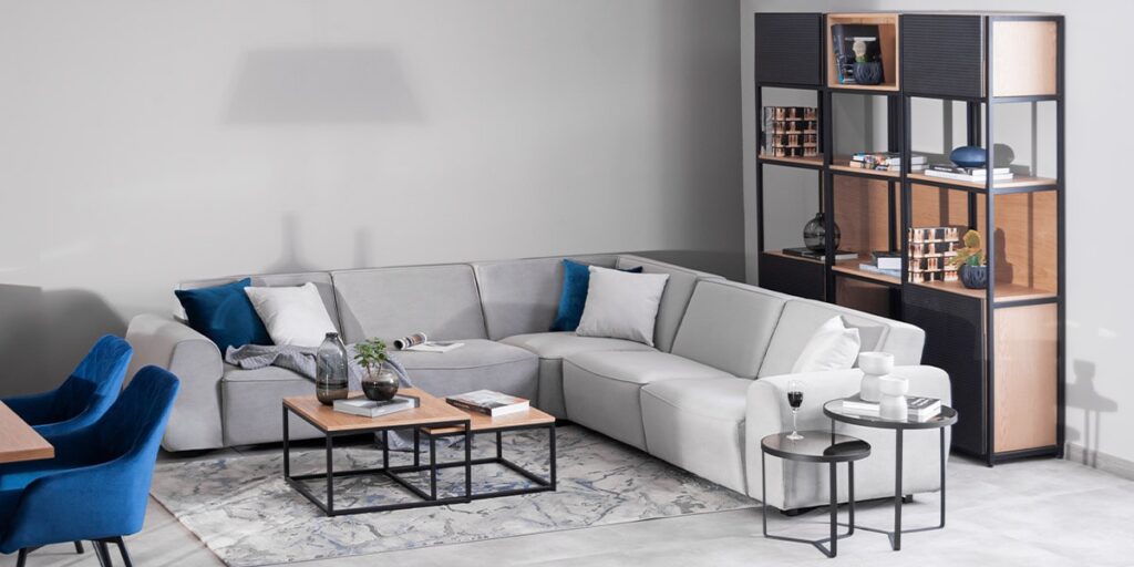 Sala con sofá modular en L gris claro, mesas de centro anidadas de madera y metal, y una estantería negra con objetos