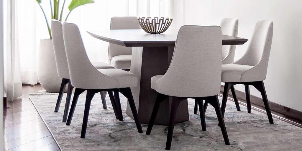 Comedor con mesa de base cónica oscura y sillas tapizadas en gris claro con patas negras, sobre un tapete gris