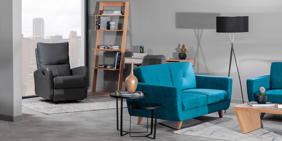 Sala con un sofá azul turquesa de dos puestos, un sillón reclinable gris oscuro, una repisa de madera y una lámpara de pie