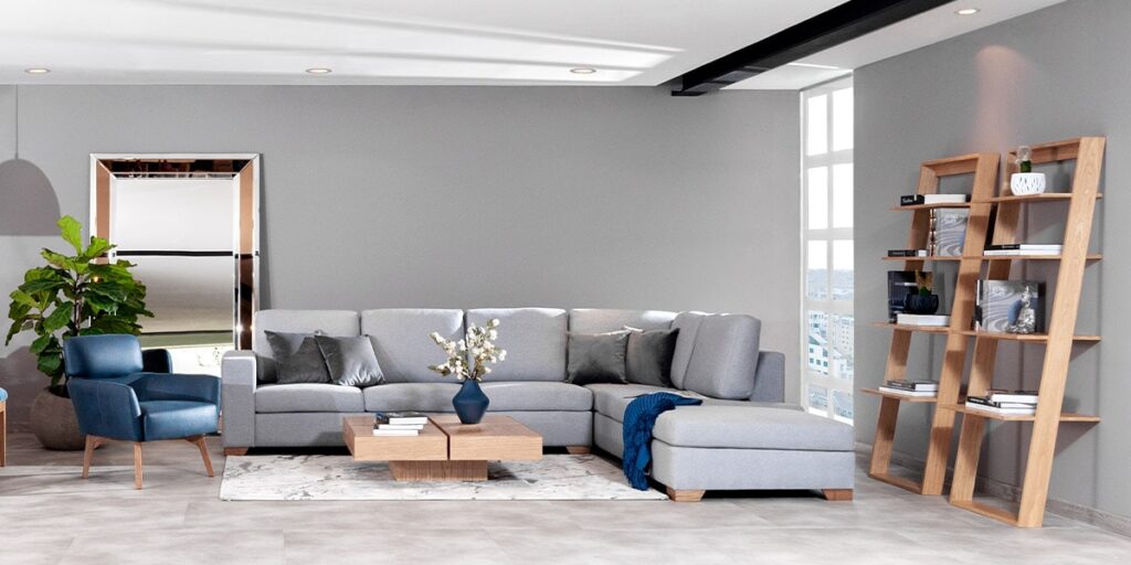 Sala con sofá modular gris, poltrona azul y repisas de madera, con una planta de hojas grandes junto a un espejo