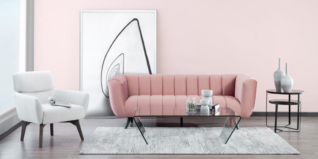 Sofá rosa palo de canales verticales y poltrona blanca con mesa de centro de vidrio, frente a un muro rosa claro