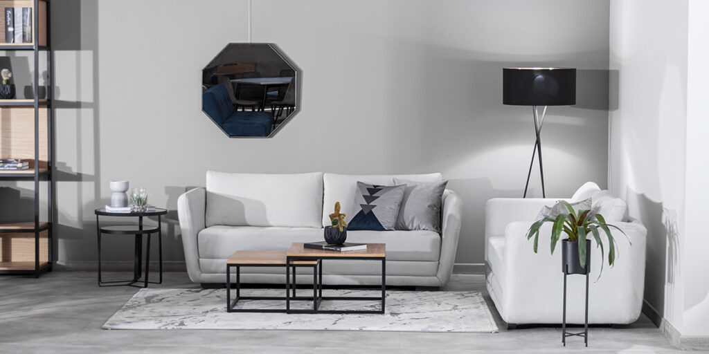 Sofá blanco de tres puestos con mesas de centro de madera y metal anidadas, una poltrona blanca y un espejo octagonal