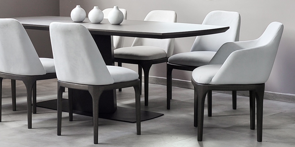 Mesa de comedor oscura con sillas tapizadas en blanco de patas negras y tres jarrones blancos