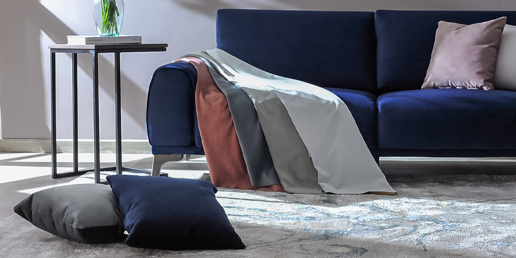 Sofá azul oscuro con manta gris y terracota, cojín rosa, mesa auxiliar negra y cojines de piso en gris y azul