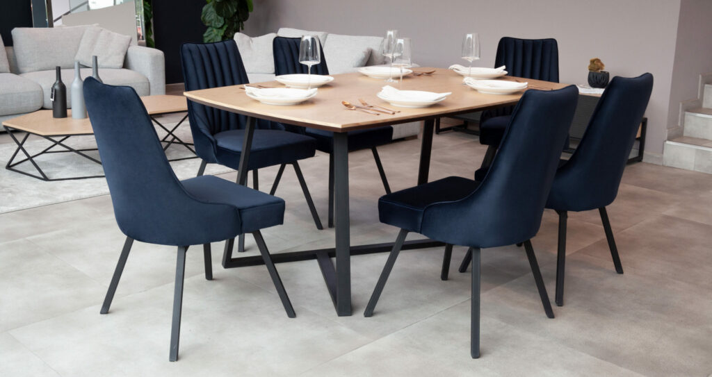 Comedor con mesa de madera clara y base negra, y seis sillas tapizadas en terciopelo azul oscuro