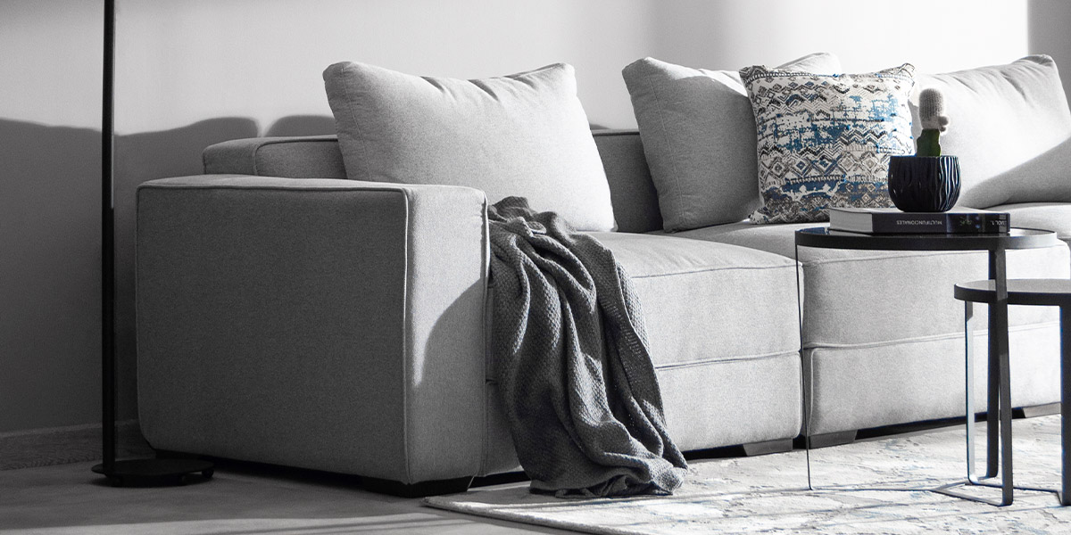 Detalle de un sofá modular gris claro con cojines estampados, una manta gris y una mesa auxiliar negra