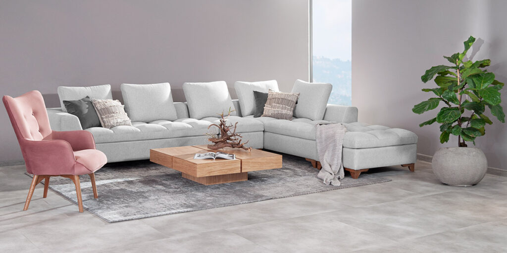 Sofá modular en L gris claro con poltrona rosa, mesa de centro de madera y una planta grande en matera