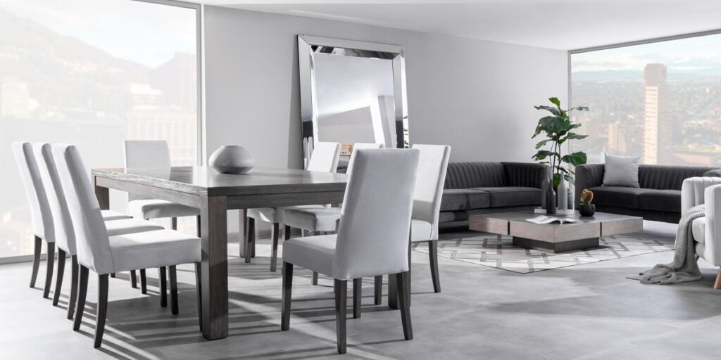Comedor con mesa de madera oscura y sillas grises claras, junto a un gran espejo de pared apoyado en el suelo y ventanales con vista a la ciudad