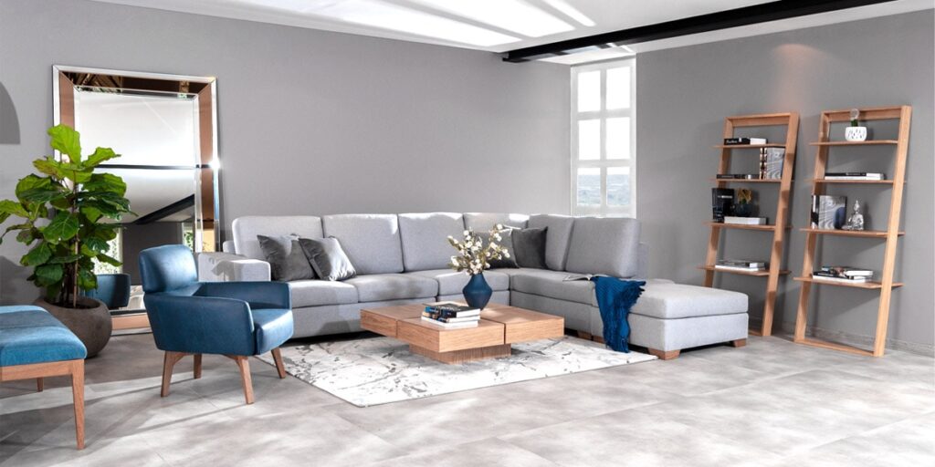 Sala amplia con sofá modular gris, poltrona azul, mesa de centro de madera y repisas de madera, junto a un ventanal