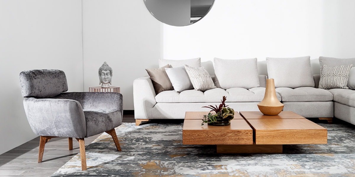 Sala con sofá modular crema, poltrona gris de terciopelo, mesa de centro de madera y una pequeña figura de Buda