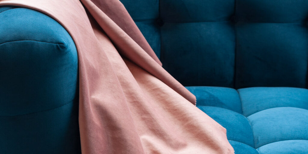 Detalle de un sofá azul turquesa tapizado en terciopelo con una manta rosa palo