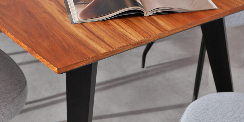 Detalle de una mesa de madera con tapa veteada y patas negras, con una revista abierta