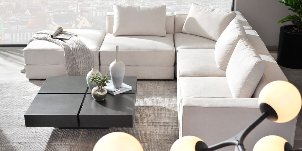 Sofá modular crema con mesa de centro negra de módulos y una lámpara de globos blancos en primer plano