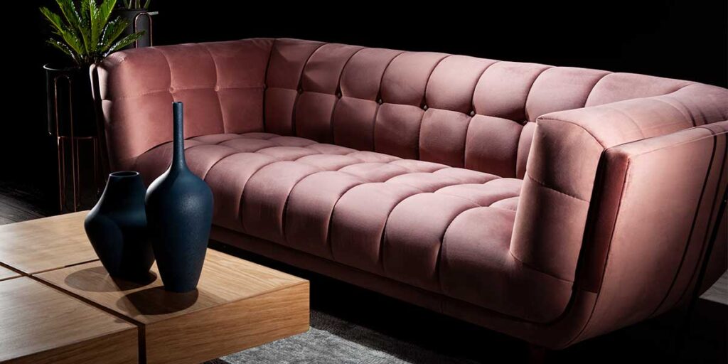 Sofá de terciopelo rosa capitoné con jarrones azul oscuro y mesa de centro de madera, sobre fondo negro