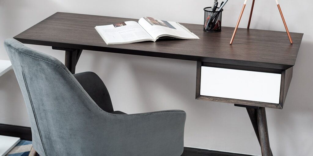 Escritorio de madera oscura con una revista abierta y un portalápices, junto a una silla de terciopelo gris azulado